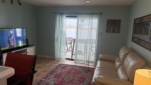 A living room with a television, a red chair, a beige sofa, a patterned rug, and a view through a glass door to the outside. - Lake View Condo Workers Escape (Port Arthur)