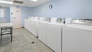A laundry room with multiple washing machines, a clock on the wall, and a door with a sign. - Lake View Condo Workers Escape (Port Arthur)