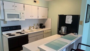 A compact kitchen with white cabinets, a microwave, a stove, a sink, and a refrigerator. - Lake View Condo Workers Escape (Port Arthur)