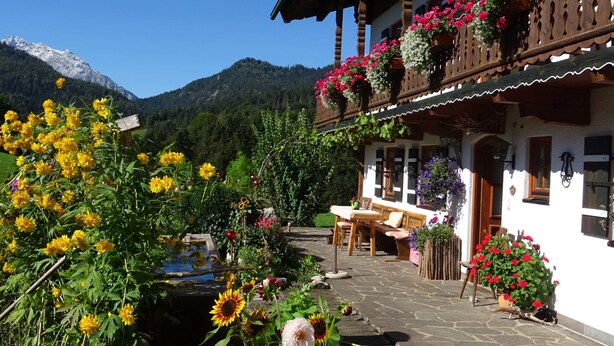 Un chalé tradicional con un patio de piedra, mobiliario de madera y jardineras en el balcón.