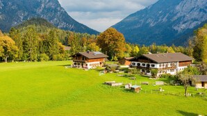 Un entorno rural con dos casas de madera rodeadas por un campo verde y montañas al fondo.