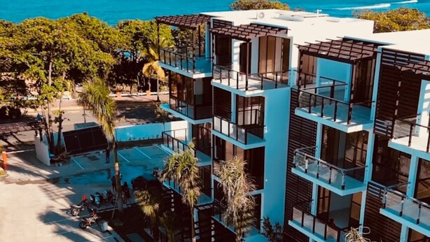 A modern multi-story building with balconies overlooking a parking area and a body of water. - Ámari, Spacious beach front 3-bedroom apartment with pool in sunny Puerto Plata (Puerto Plata)