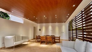 A spacious room with a high ceiling, a wooden ceiling, a dining table with chairs, a white sofa, and a window with blinds. - Ámari, Spacious beach front 3-bedroom apartment with pool in sunny Puerto Plata (Puerto Plata)