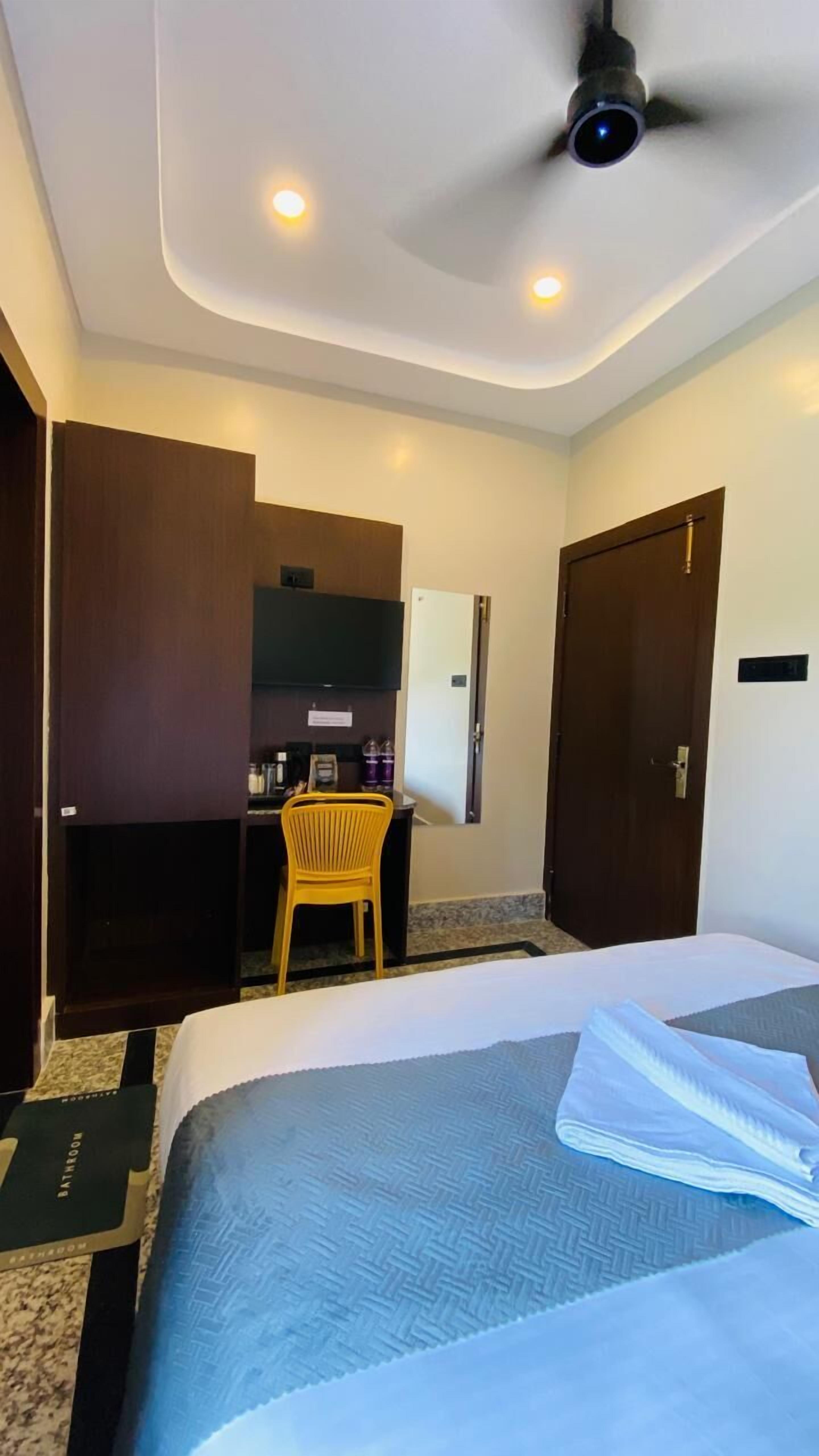 A hotel room with a bed, a desk, a chair, a wardrobe, and a ceiling fan.