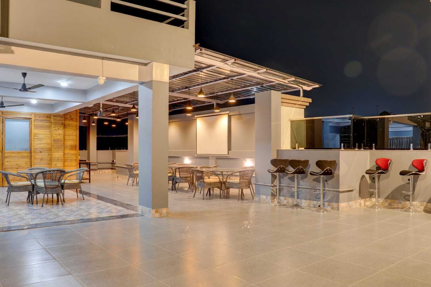 Un espacio interior moderno con varias zonas de estar, incluyendo mesas redondas y taburetes de bar, y una pantalla grande para presentaciones.