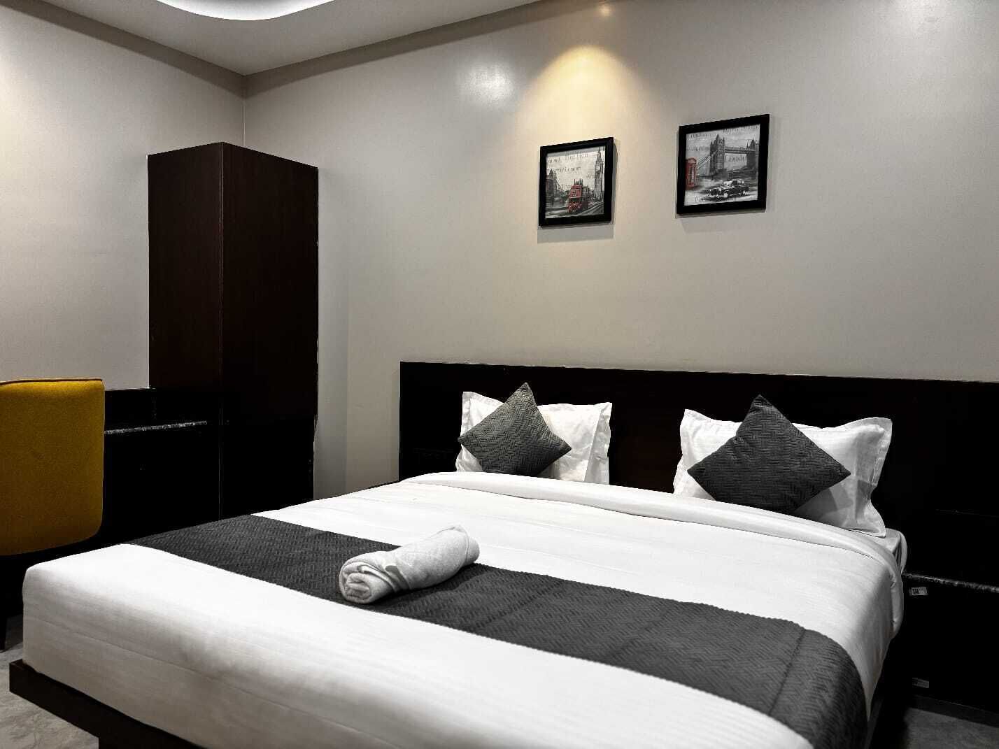 A hotel room with a large bed, a wardrobe, and two framed pictures on the wall.