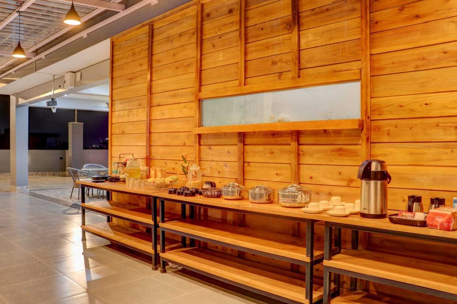 Une longue table en bois, avec des bancs, un coin café et une vue sur la ville la nuit.
