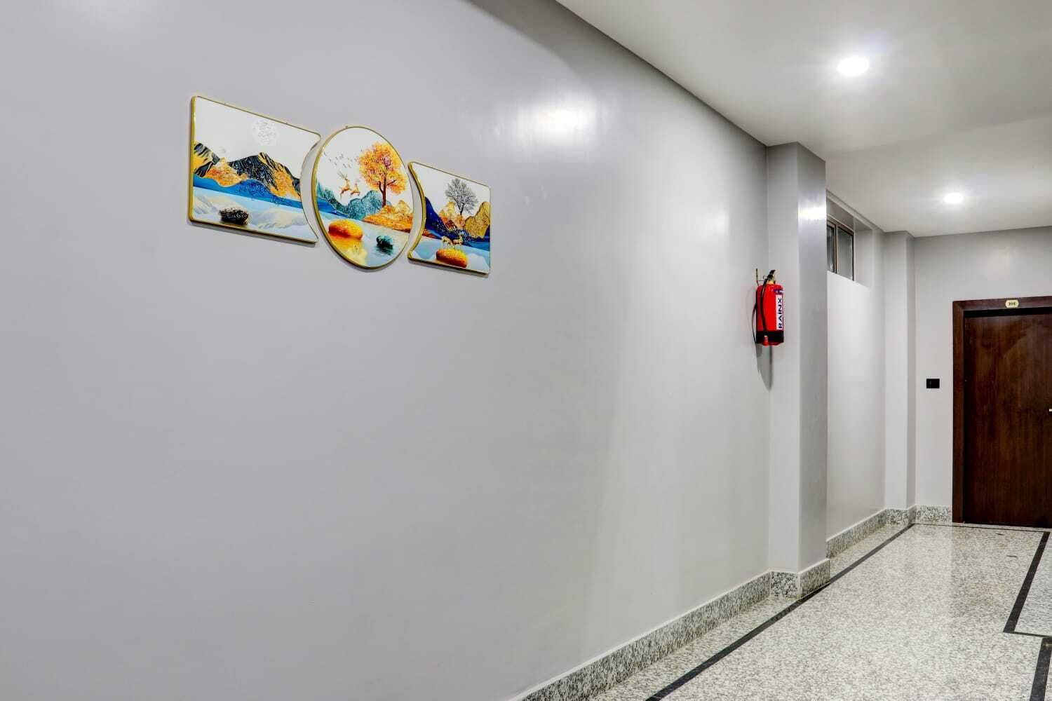 Un pasillo con tres cuadros enmarcados, un extintor y una puerta.