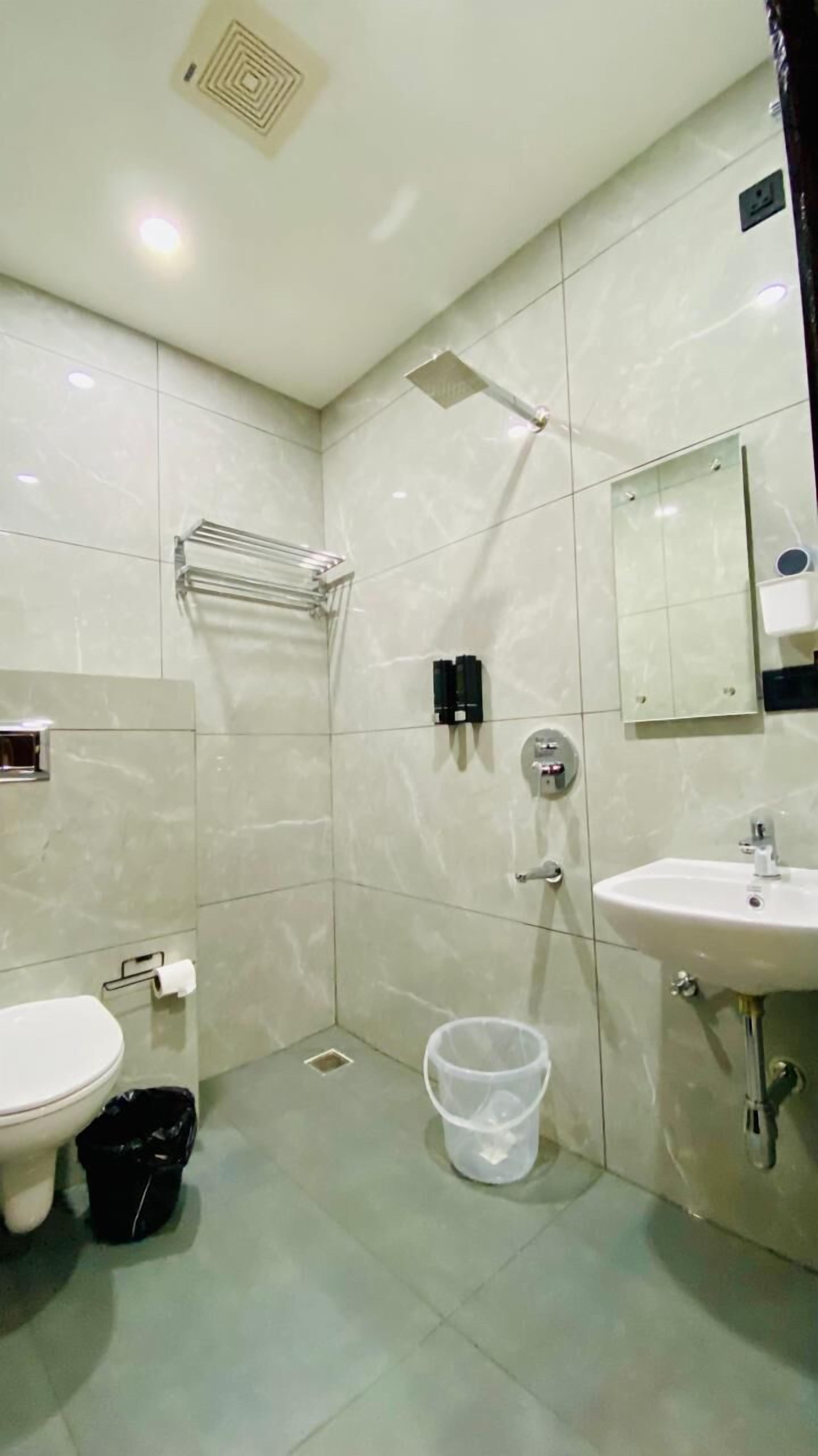 A bathroom with a toilet, sink, shower, and a trash bin.