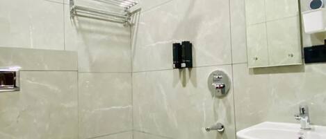 A bathroom with a toilet, sink, shower, and a trash bin.