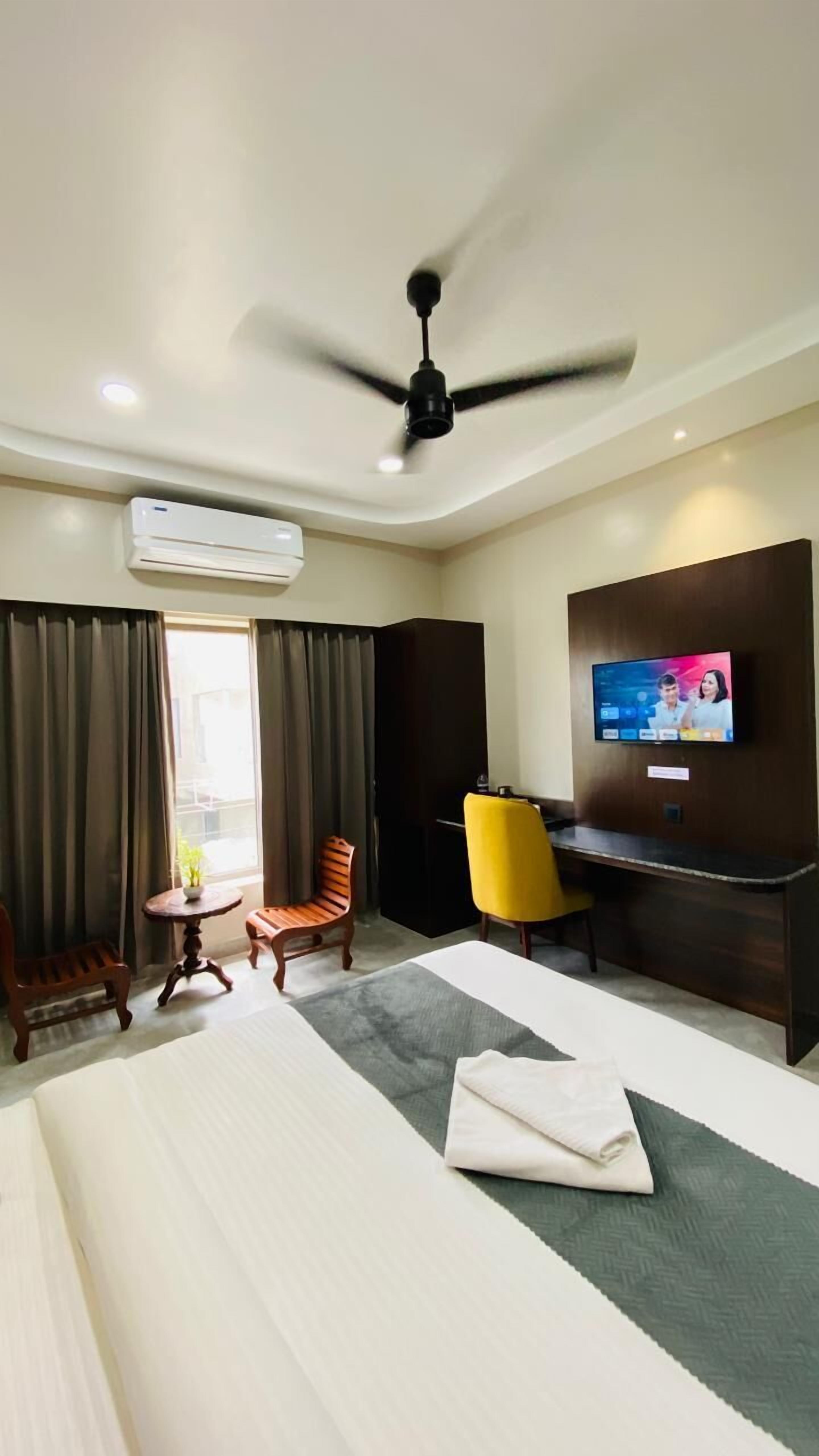 Ein Hotelzimmer mit Bett, Schreibtisch, Fernseher, Deckenventilator und Klimaanlage.