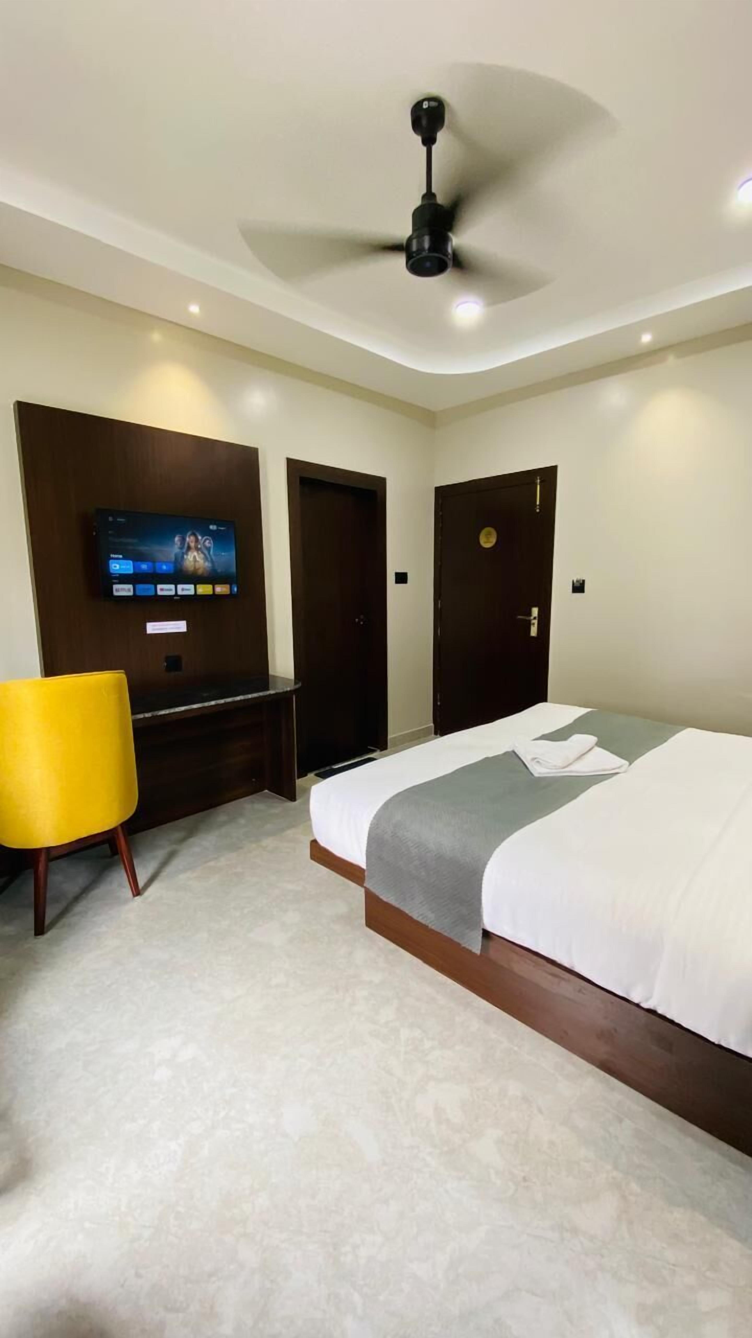 A hotel room with a bed, a TV mounted on the wall, a ceiling fan, and two doors.