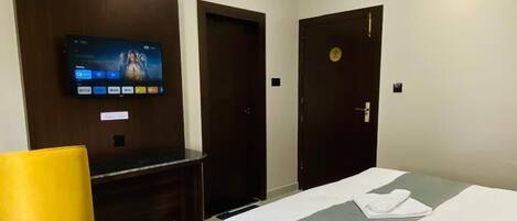 A hotel room with a bed, a TV mounted on the wall, a ceiling fan, and two doors.