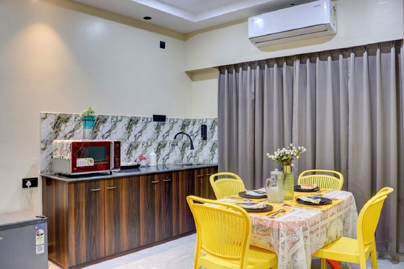 Uma cozinha compacta com micro-ondas, pia e área de refeições com cadeiras amarelas e mesa posta para dois.