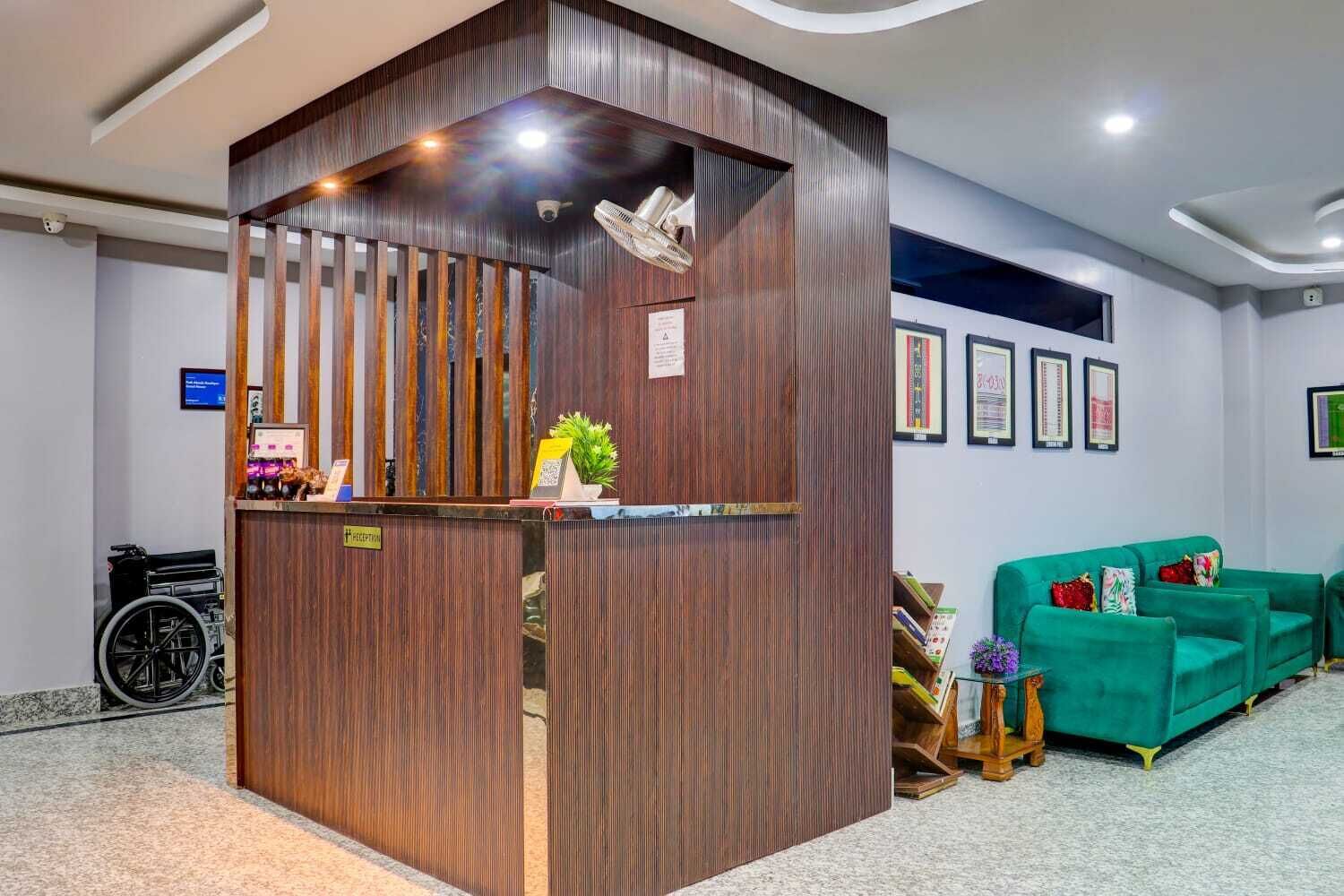Een receptiebalie met een houten afwerking, een rolstoel, een groene bank en ingelijste certificaten aan de muur.
