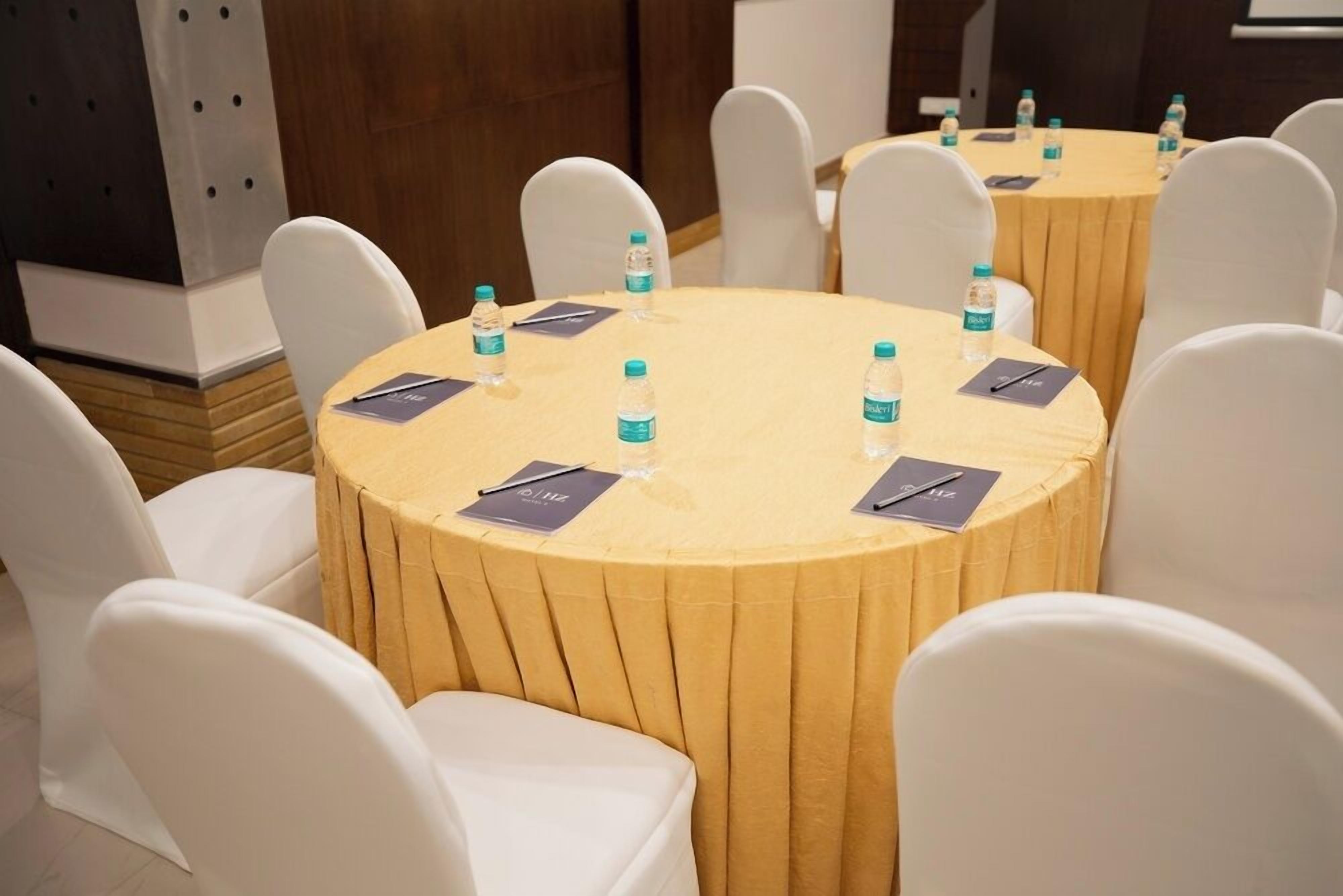 Un salón de conferencias con mesas redondas, sillas blancas y botellas de agua sobre las mesas.