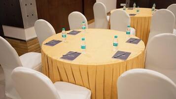 Un salón de conferencias con mesas redondas, sillas blancas y botellas de agua sobre las mesas.