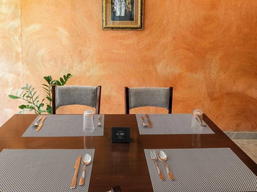 Un'area pranzo con un tavolo di legno apparecchiato per due persone, due sedie, un quadro appeso alla parete e una pianta a sinistra.