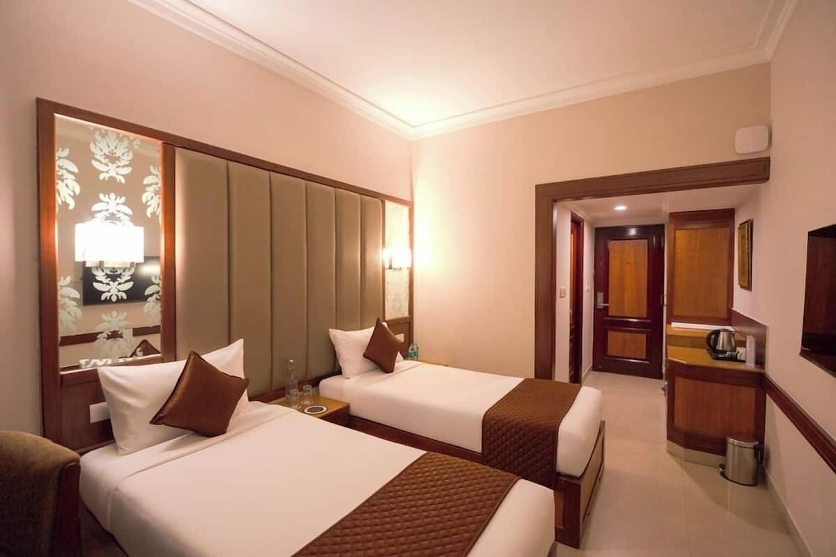 Une chambre d’hôtel avec deux lits, un coin salon, une kitchenette et un miroir orné de motifs floraux.