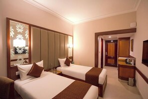 Hotelkamer met twee bedden, een zithoek, een kitchenette en een spiegel met bloemenmotief.