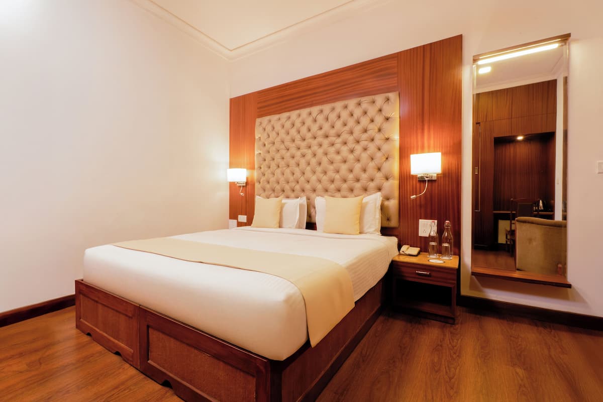 Une chambre d’hôtel avec un grand lit, une tête de lit en bois, des lampes de chevet, une table de chevet et un miroir.