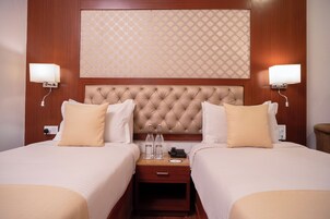 A hotel room with two beds, a wooden headboard, bedside lamps, a nightstand, and a patterned wall.