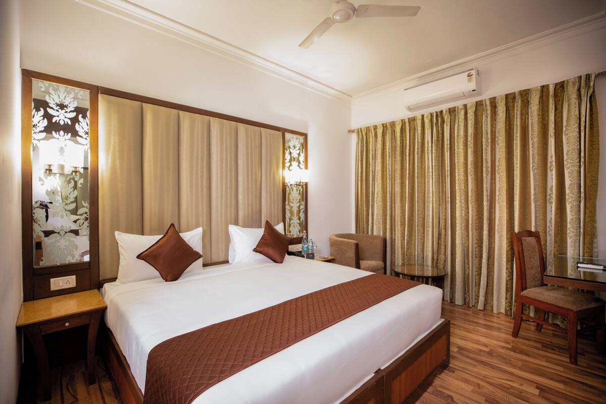 Une chambre d’hôtel avec un grand lit, un bureau, une chaise, une table et un ventilateur de plafond.