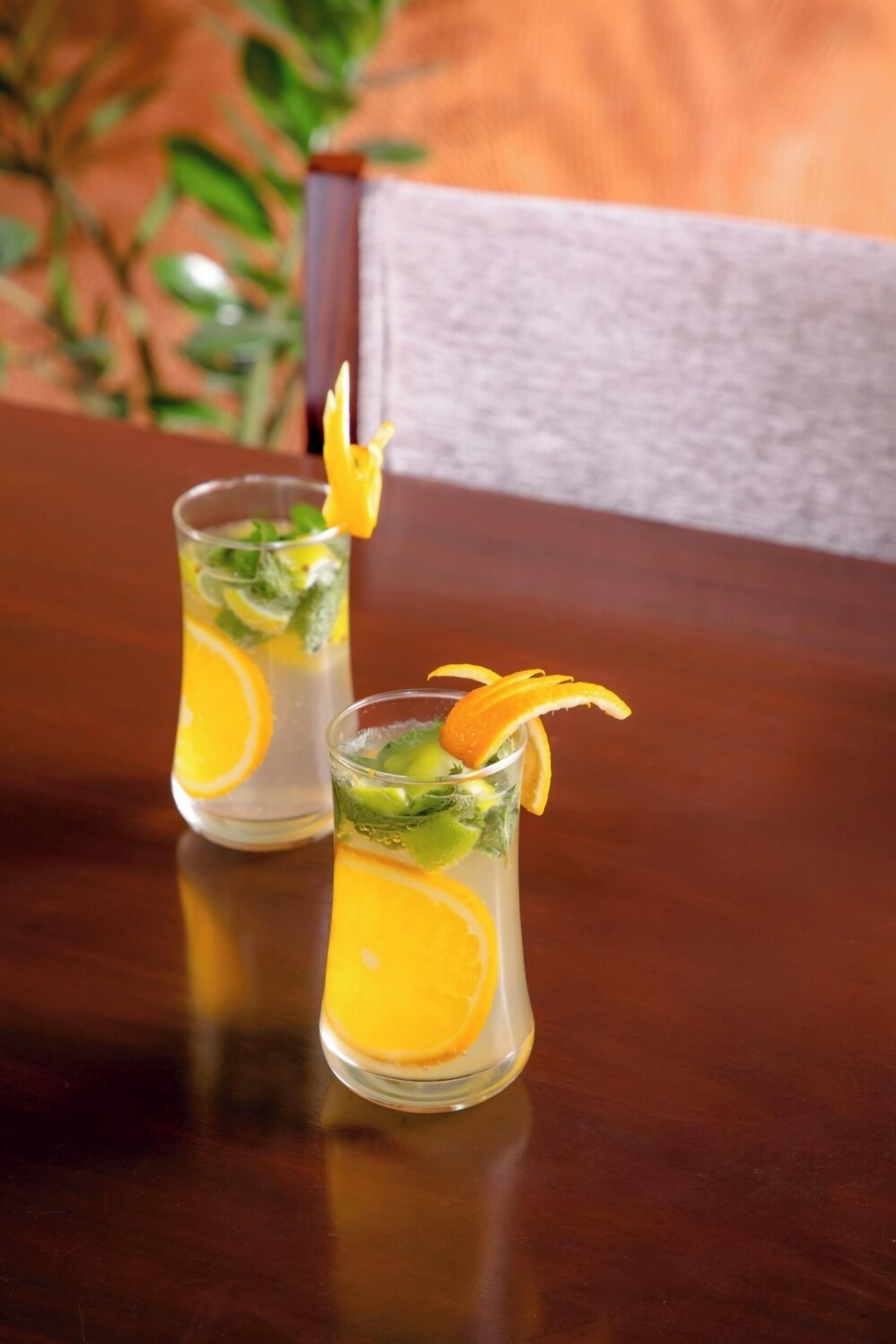 Two glasses of a citrus drink with orange slices and mint leaves, placed on a wooden table.