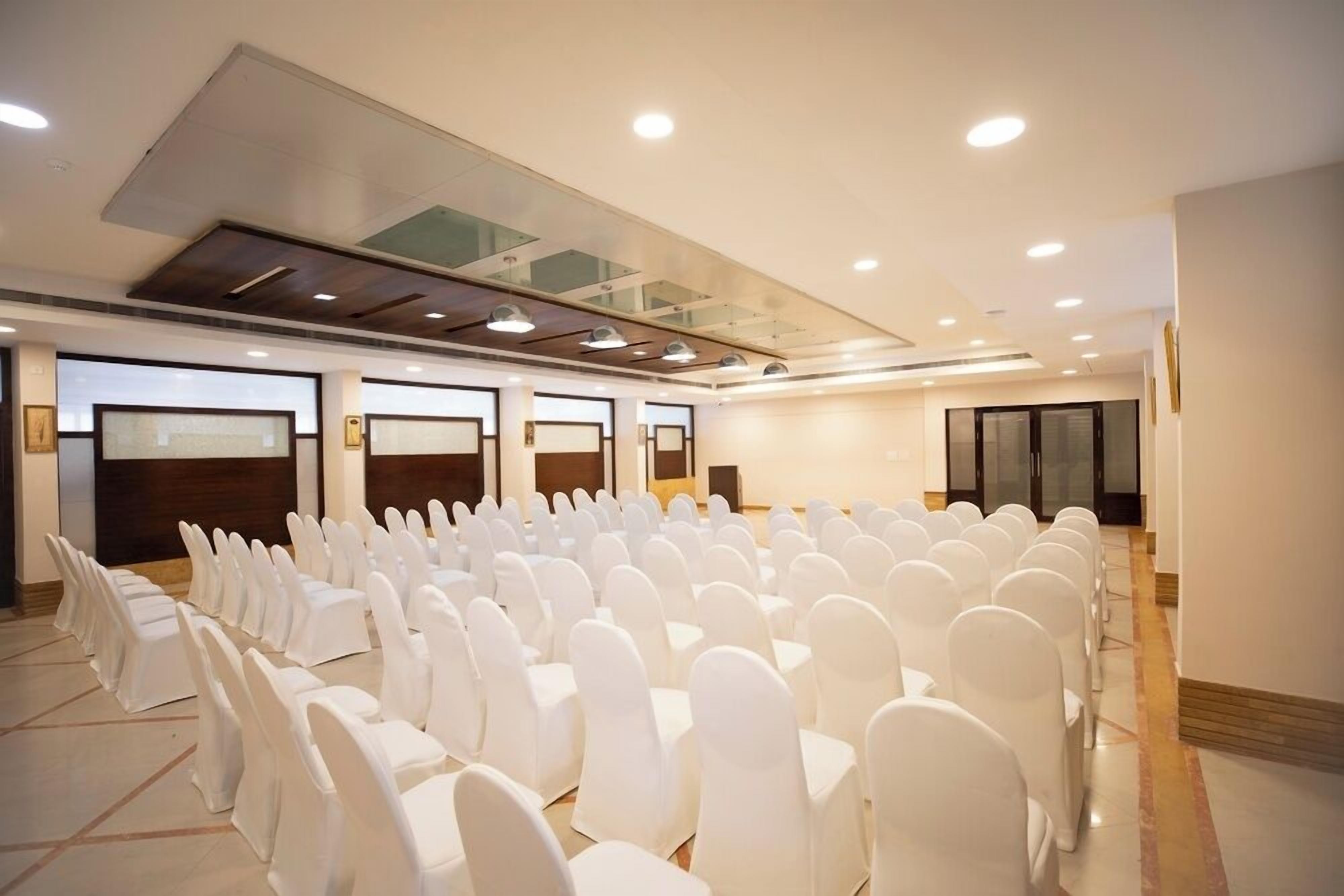 Un salón de conferencias con filas de sillas blancas, techo de vidrio y una zona escenario.