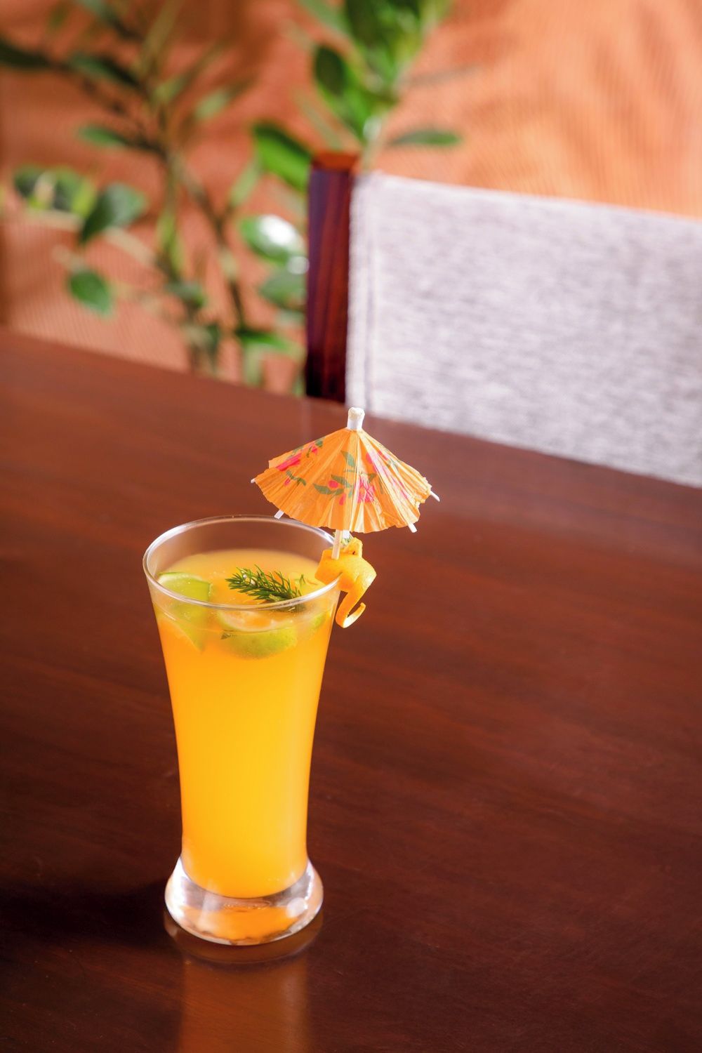 Un vaso alto con una bebida amarilla, decorado con una sombrilla pequeña y una rodaja de fruta, sobre una mesa de madera.