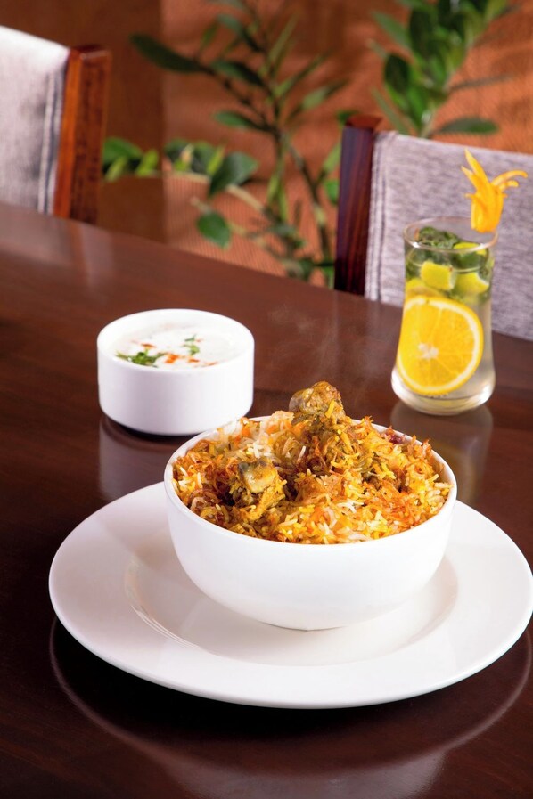 A bowl of biryani on a white plate with a small bowl of raita in the background. - U by Z Hotels, Richmond Circle (Bengaluru)