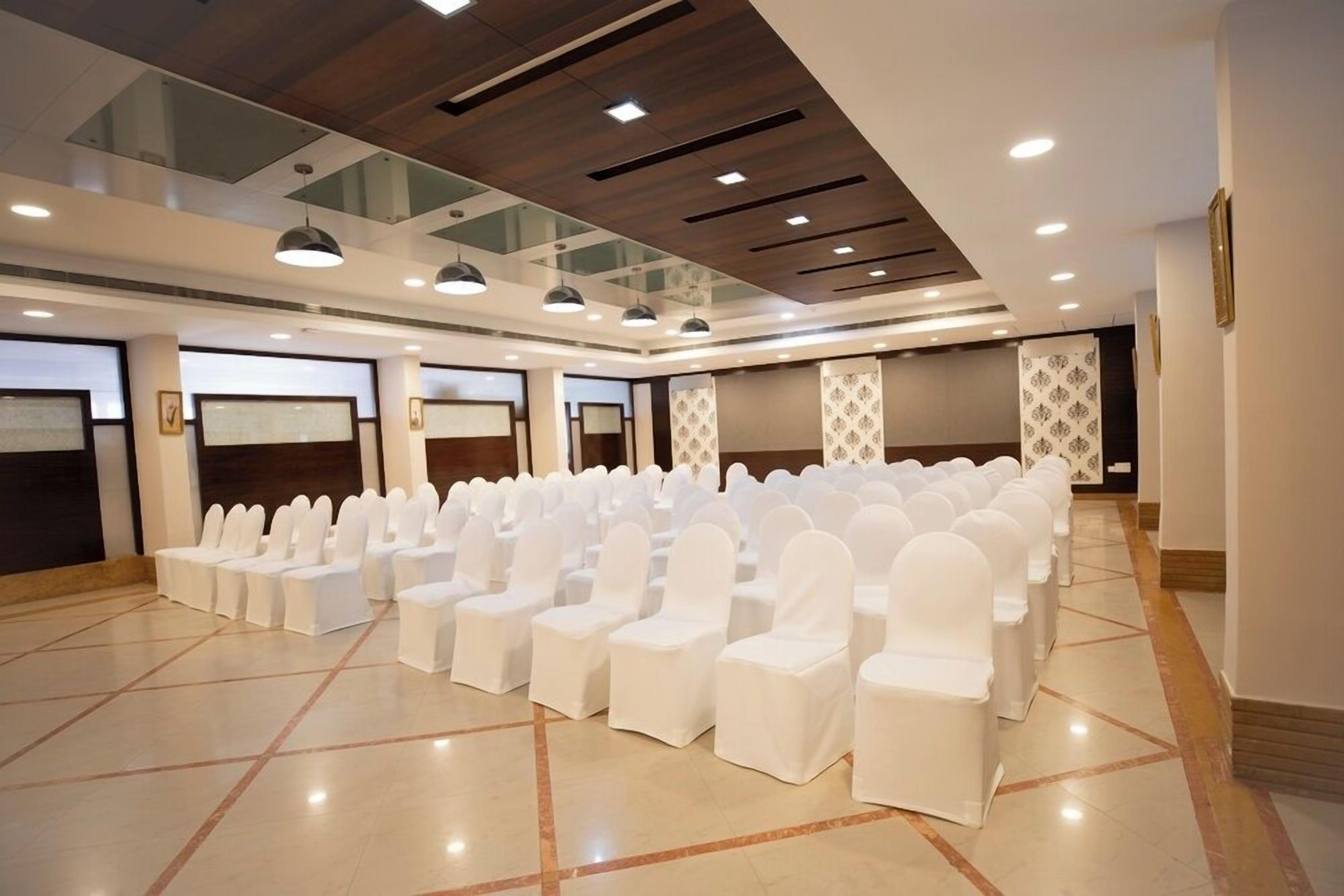 Un salón de conferencias con filas de sillas blancas, piso pulido y un diseño moderno de techo.