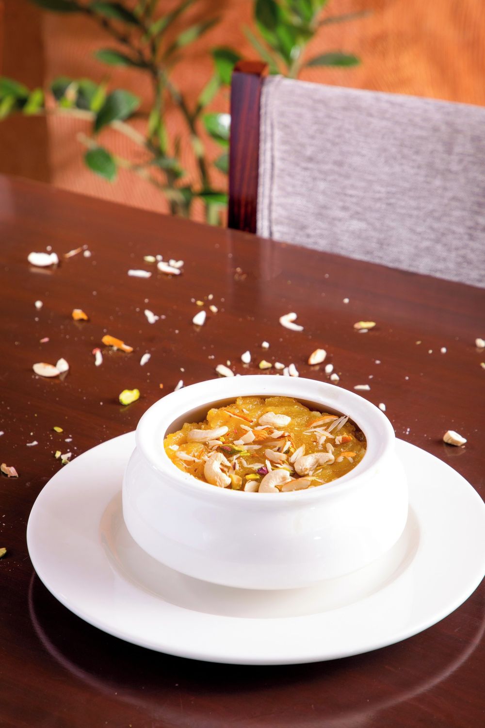 Un bol blanco de postre sobre un plato blanco, colocado sobre una mesa de madera con nueces esparcidas.