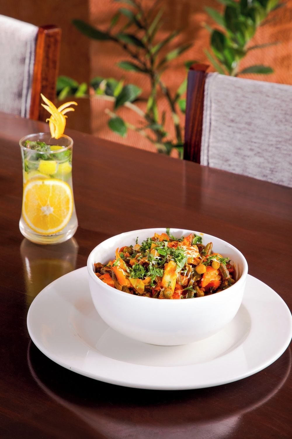 A bowl of food on a white plate with a glass of orange juice beside it.