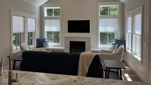 A spacious living room with a fireplace, large windows with blinds, a sofa, and a television. - Pine Cottage Big Glen Lake Private Access (Maple City)