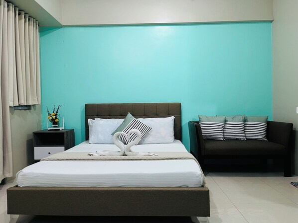 A neatly arranged bedroom with a bed, a nightstand, a sofa, and a wall with teal paint. - One Palm Tree Villas (Pasay)