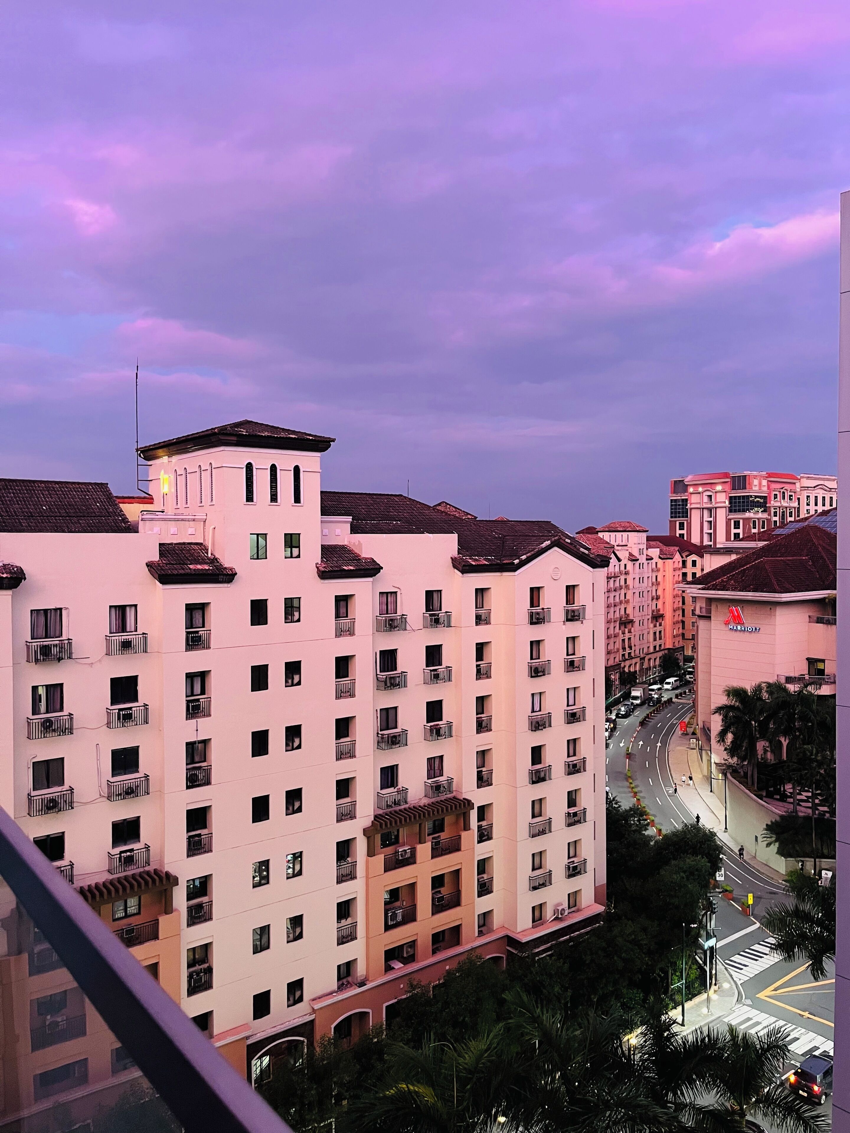 A multi-story hotel with balconies, a Marriott logo, and a view of a city street with palm trees.