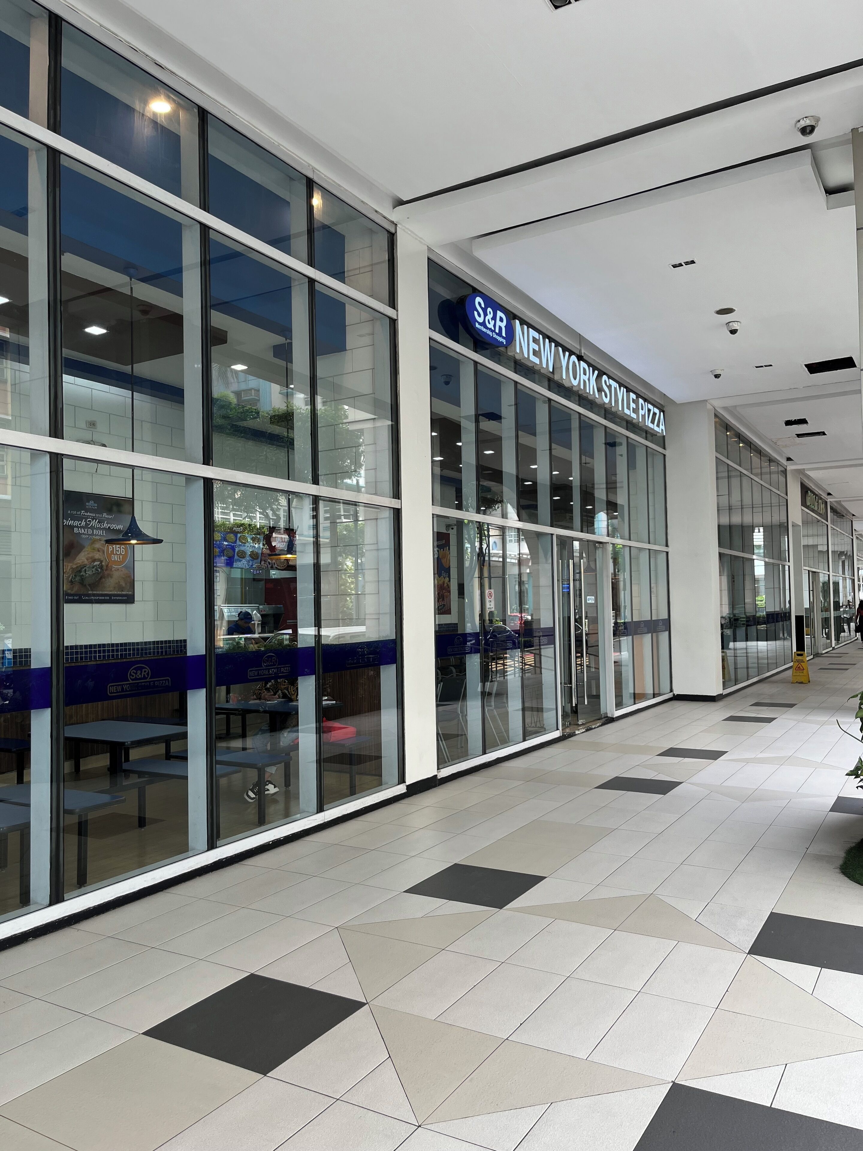 A New York style pizza restaurant with a modern glass facade and a tiled floor.