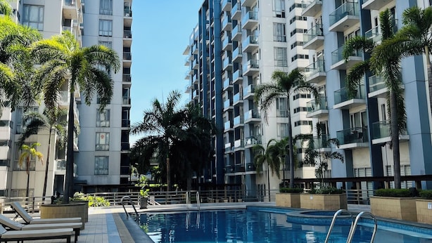 A modern apartment building with a swimming pool, palm trees, and a clear sky. - One Palm Tree Villas (Pasay)