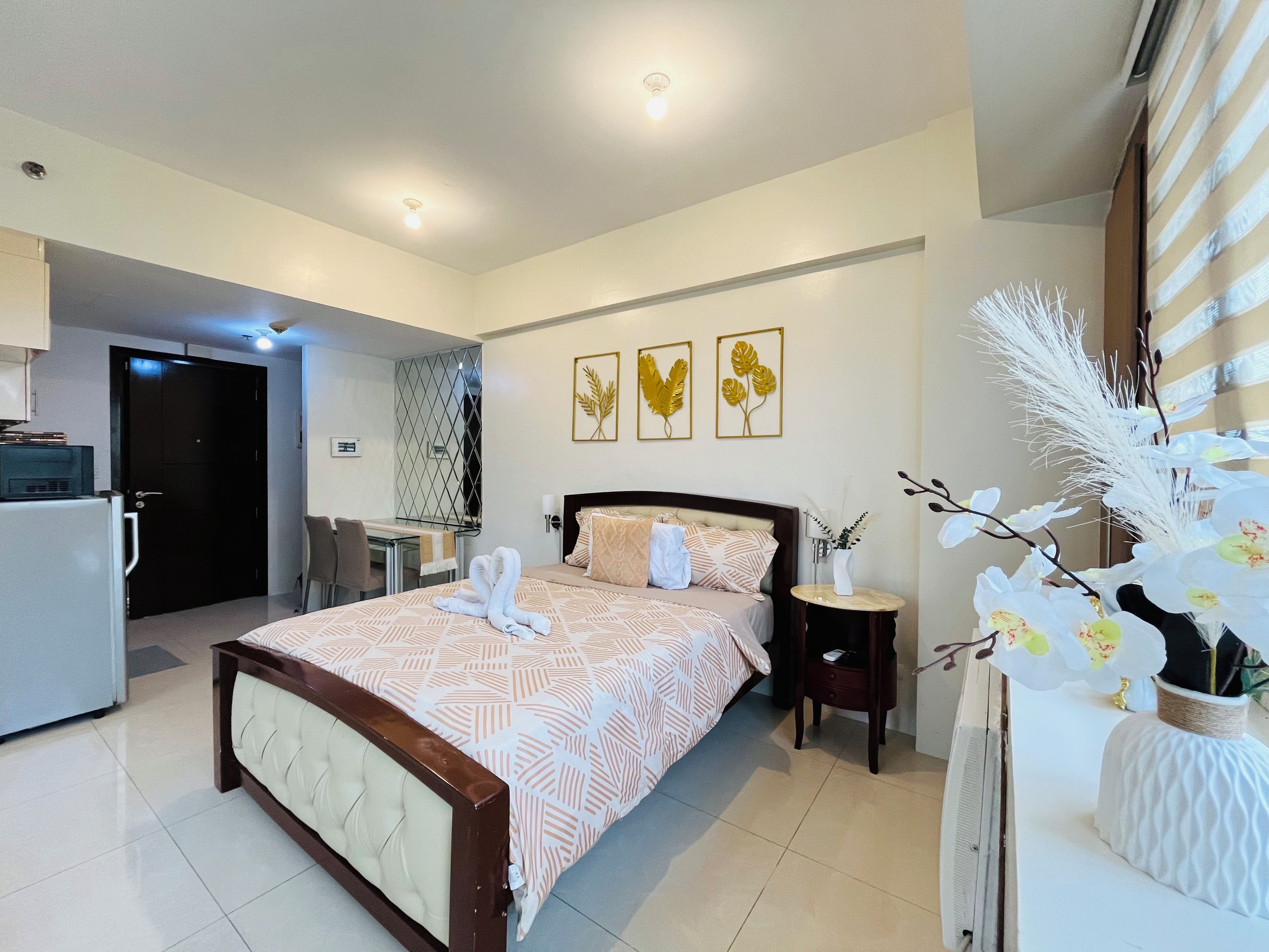 Habitación de hotel con cama, escritorio, silla, mesita y una planta decorativa.