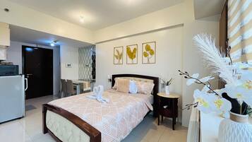 Habitación de hotel con cama, escritorio, silla, mesita y una planta decorativa.