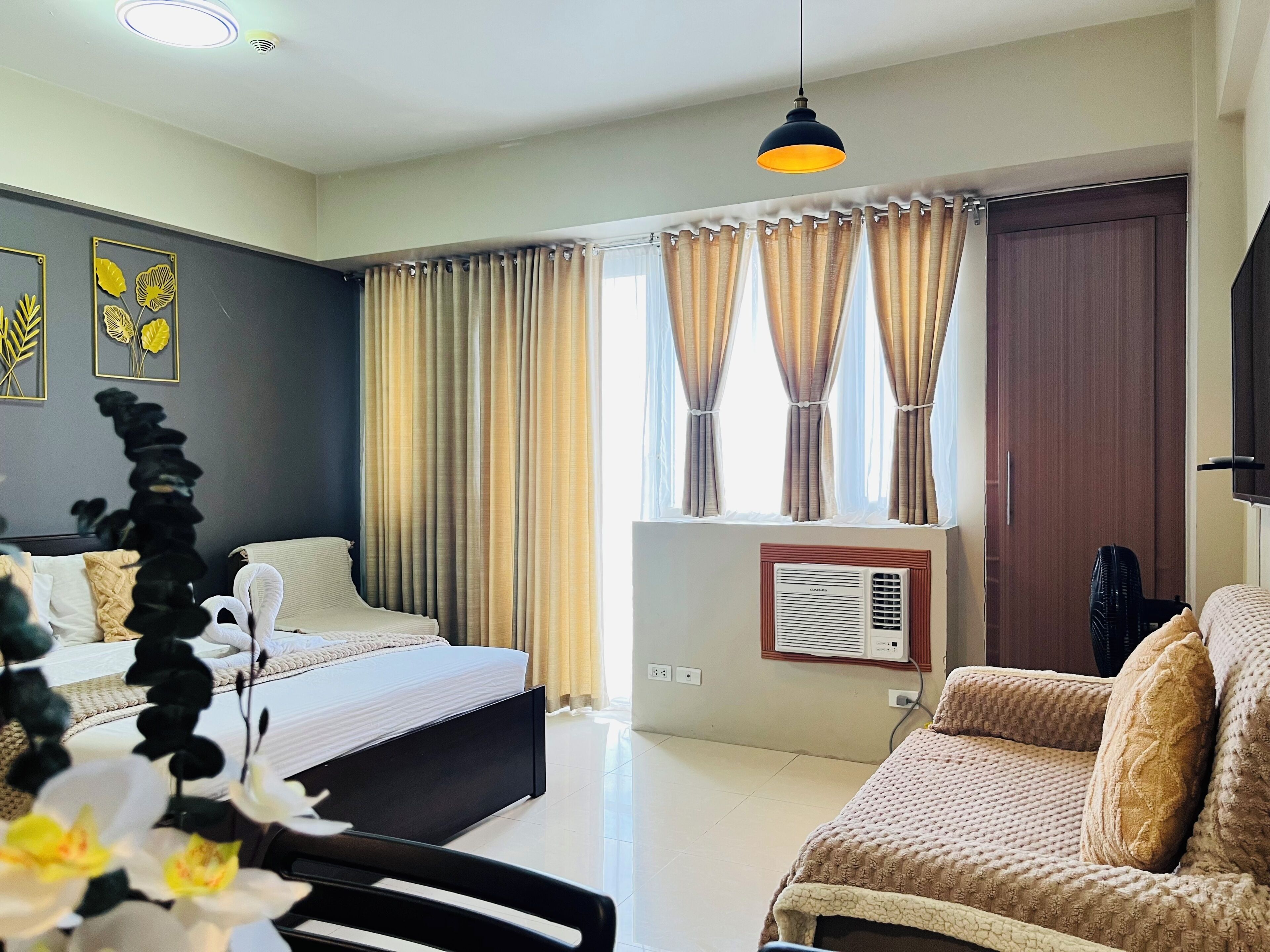 A hotel room with a bed, a sofa, a desk, and a window with curtains.