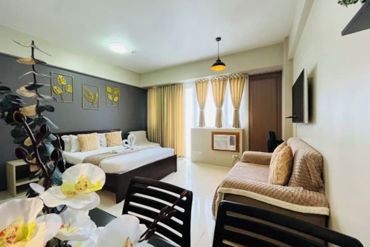 A hotel room with a bed, a sofa, a dining table, and a TV.
