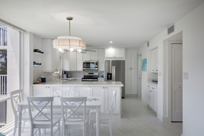 Uma cozinha moderna com armários brancos, uma ilha central com assentos e eletrodomésticos embutidos.