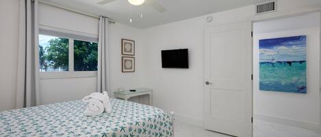 Une chambre d’hôtel avec un lit, un ventilateur de plafond, une télévision, un tableau et une fenêtre avec des rideaux.