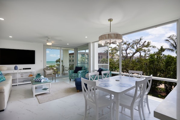 Sala moderna com TV, assentos e área de refeições com vista para o exterior.