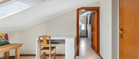 A room with a sloped ceiling, a wooden dining table, a chair, and a white desk.
