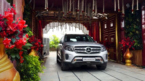 Un Mercedes-Benz plateado estacionado bajo un arco decorativo con cortinas rojas y adornos colgantes.