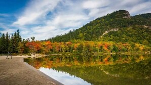 A serene lakeside scene with a clear reflection, surrounded by autumn-colored trees and a mountain in the background. - Cranmore Ski Retreat • Arcade + Firepit + Dogs OK! (Conway)