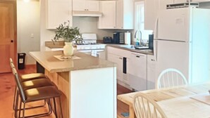 A modern kitchen with white cabinets, a central island, and a dining area with a table and chairs. - Cranmore Ski Retreat • Arcade + Firepit + Dogs OK! (Conway)